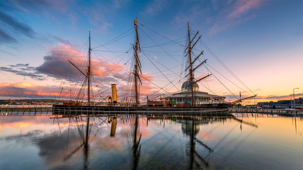 RRS Discovery at sunset from the waterside, with the vessel mirrored perfectly in the still water's reflection.