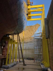 Looking up at the underside of RRS Discovery from inside the dock. A yellow steel structure supports the ship.